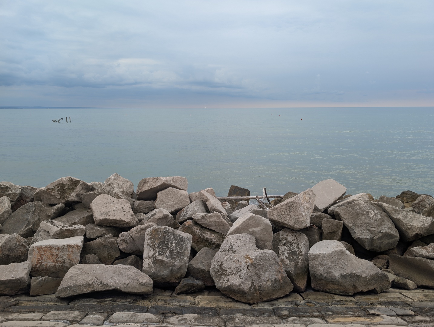 A picture of the sea and some clouds in pastel colours. Some wave breaking rocks are in front of the sea.